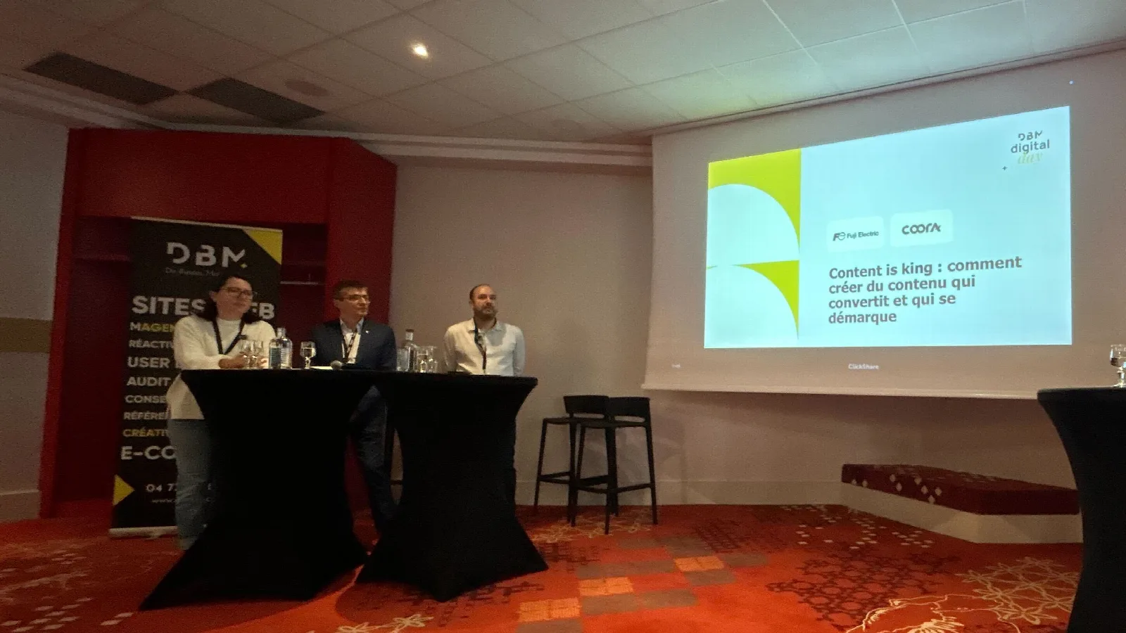 Sur scène, Caroline Brun, Stéphane Montbrizon et Raphaël Condamin devant l'écran de la conférence « Content is king », avec les logos Fuji Electric et Coora
